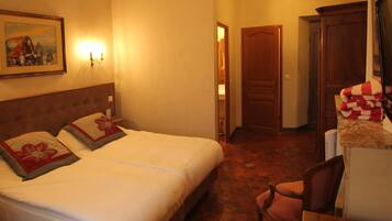 A hotel room with a bed, a chair, a desk, and a painting on the wall.