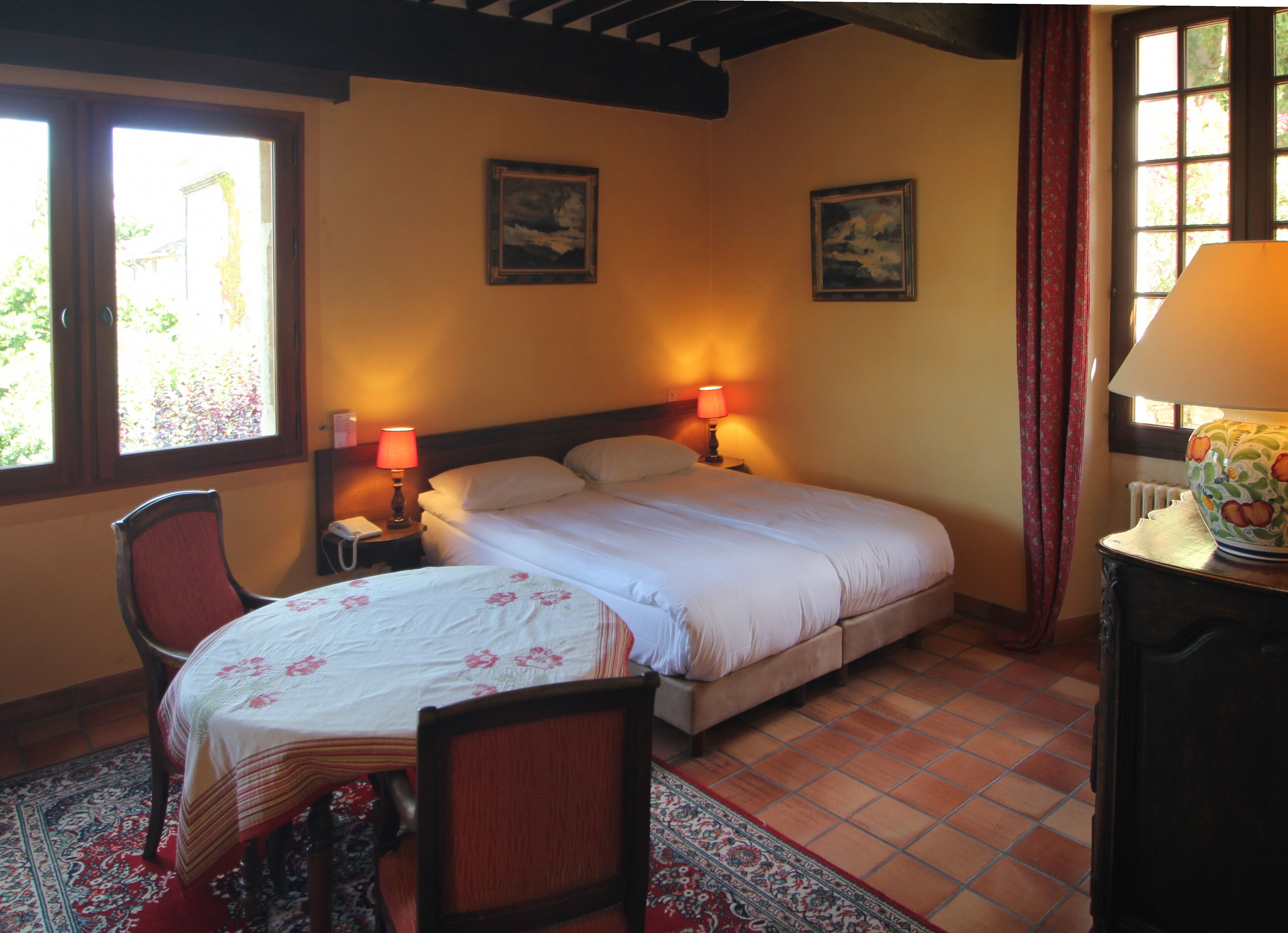 A bedroom with a bed, two bedside lamps, a chair, a table, and two paintings on the wall.