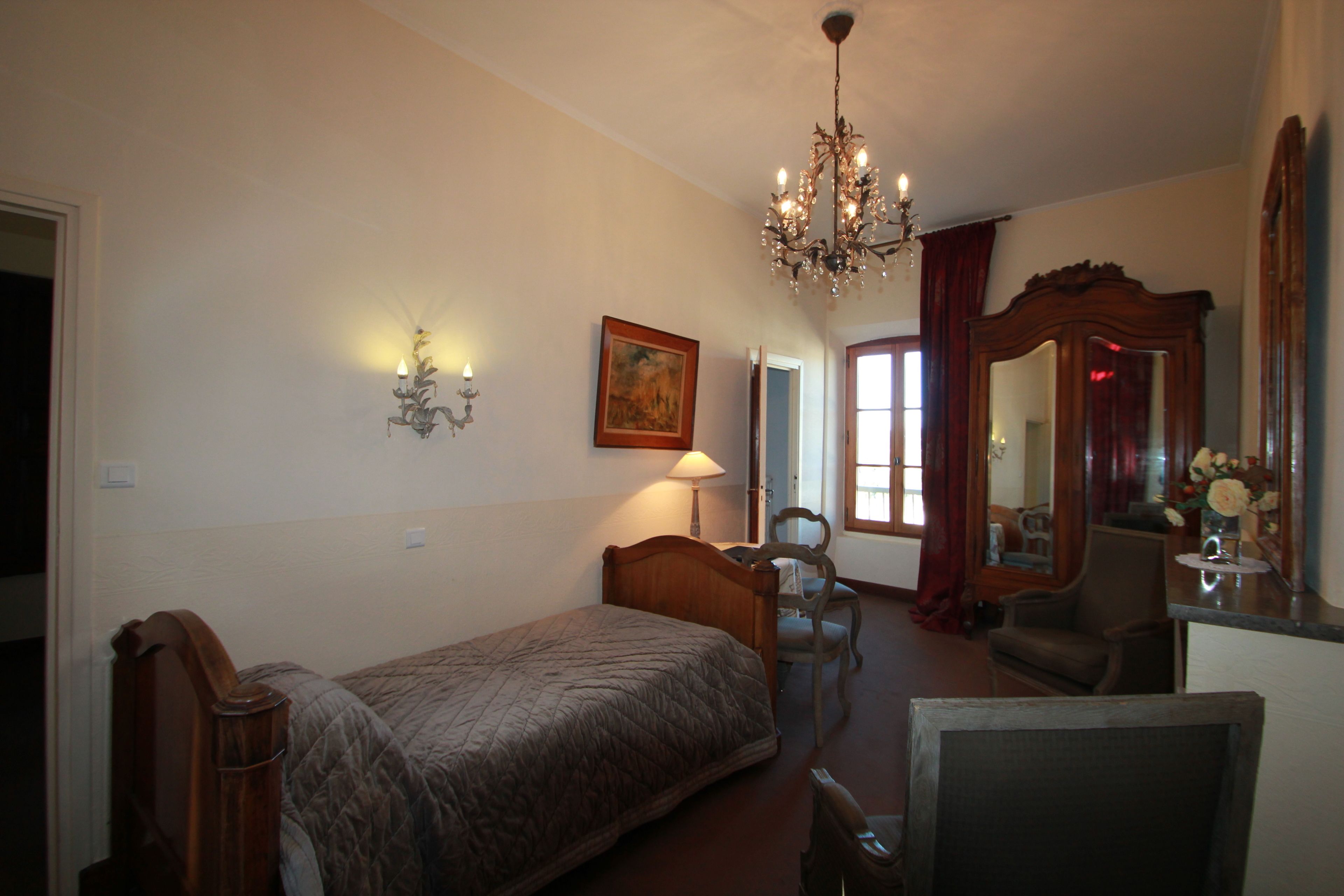 A bedroom with a bed, a chair, a desk, a mirror, and a chandelier.