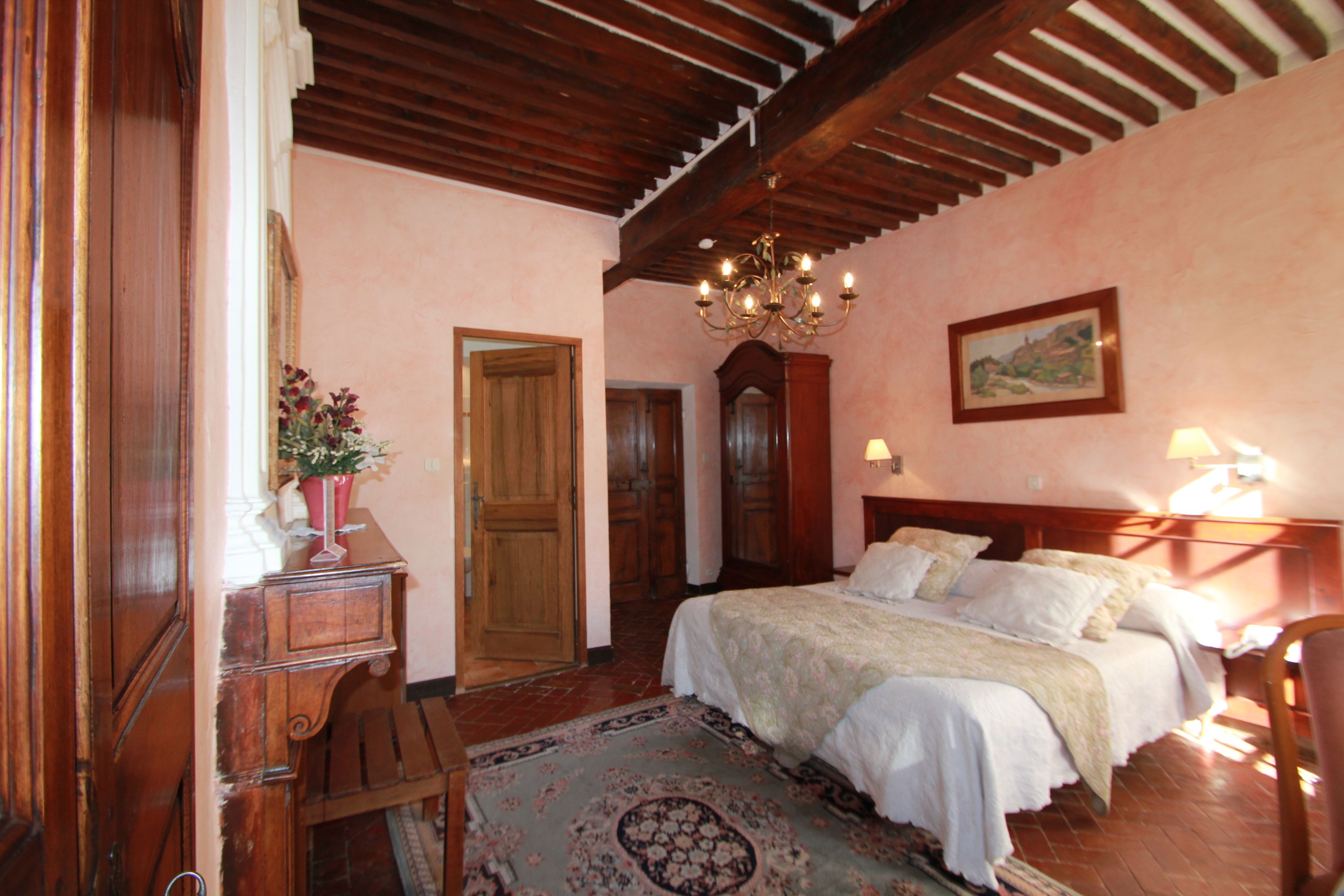 A bedroom with a wooden ceiling, a large bed, a chandelier, and a painting on the wall.