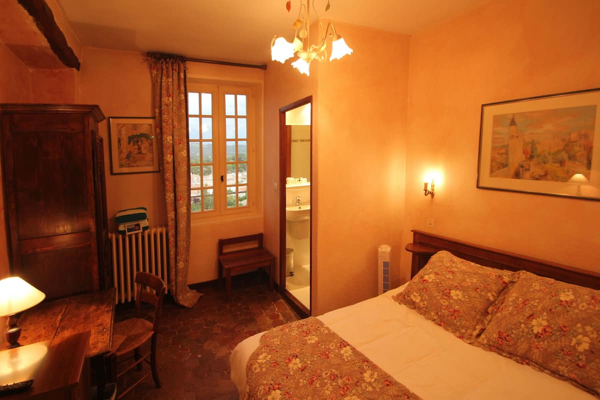 Une chambre confortable avec un grand lit, un bureau en bois avec une lampe, une chaise, un radiateur et une fenêtre avec des rideaux.