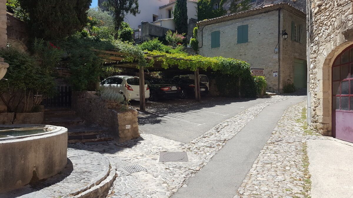 A narrow cobblestone street with parked cars and a building with a stone facade.