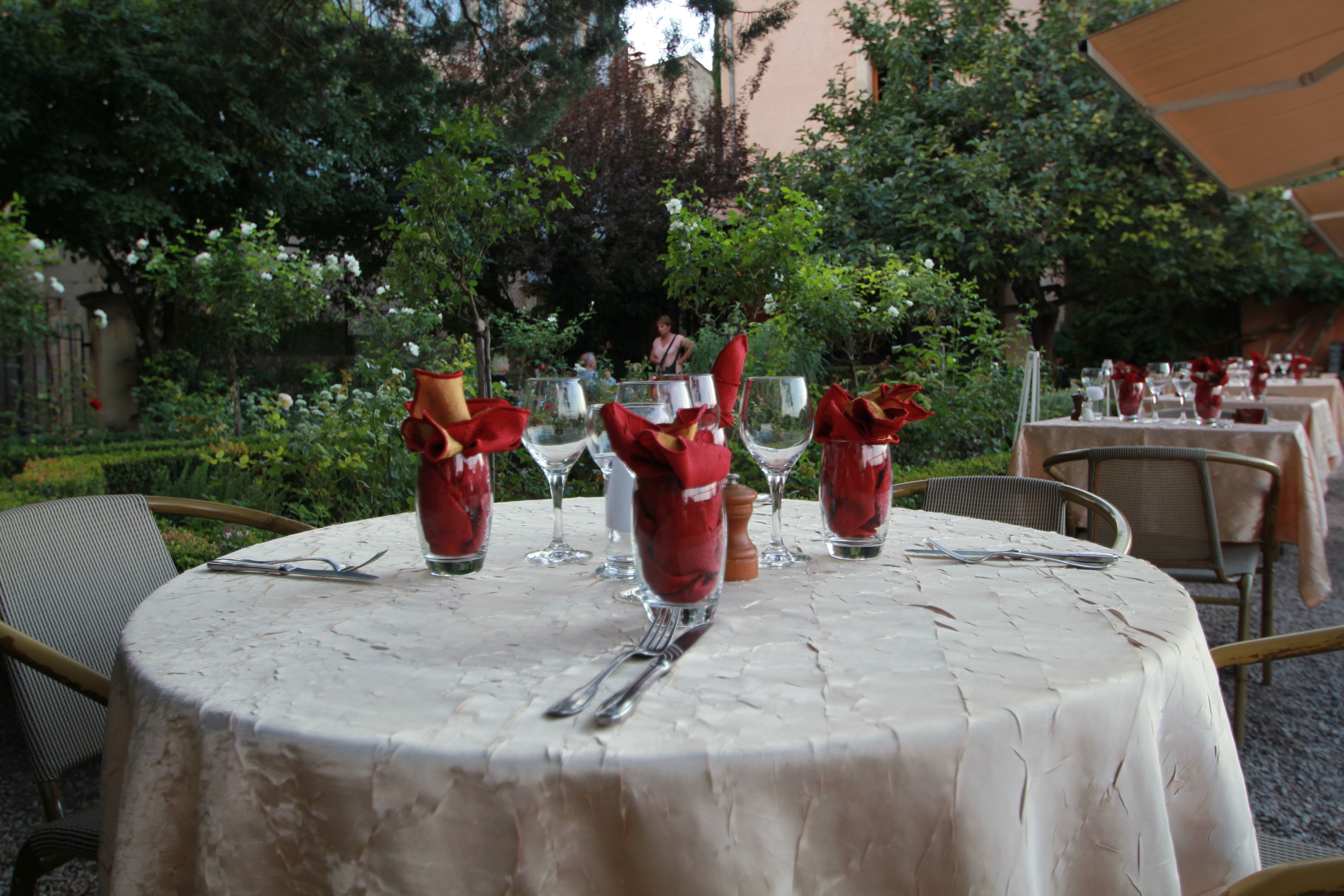 A round table with a white tablecloth, set with red napkins, wine glasses, and cutlery.