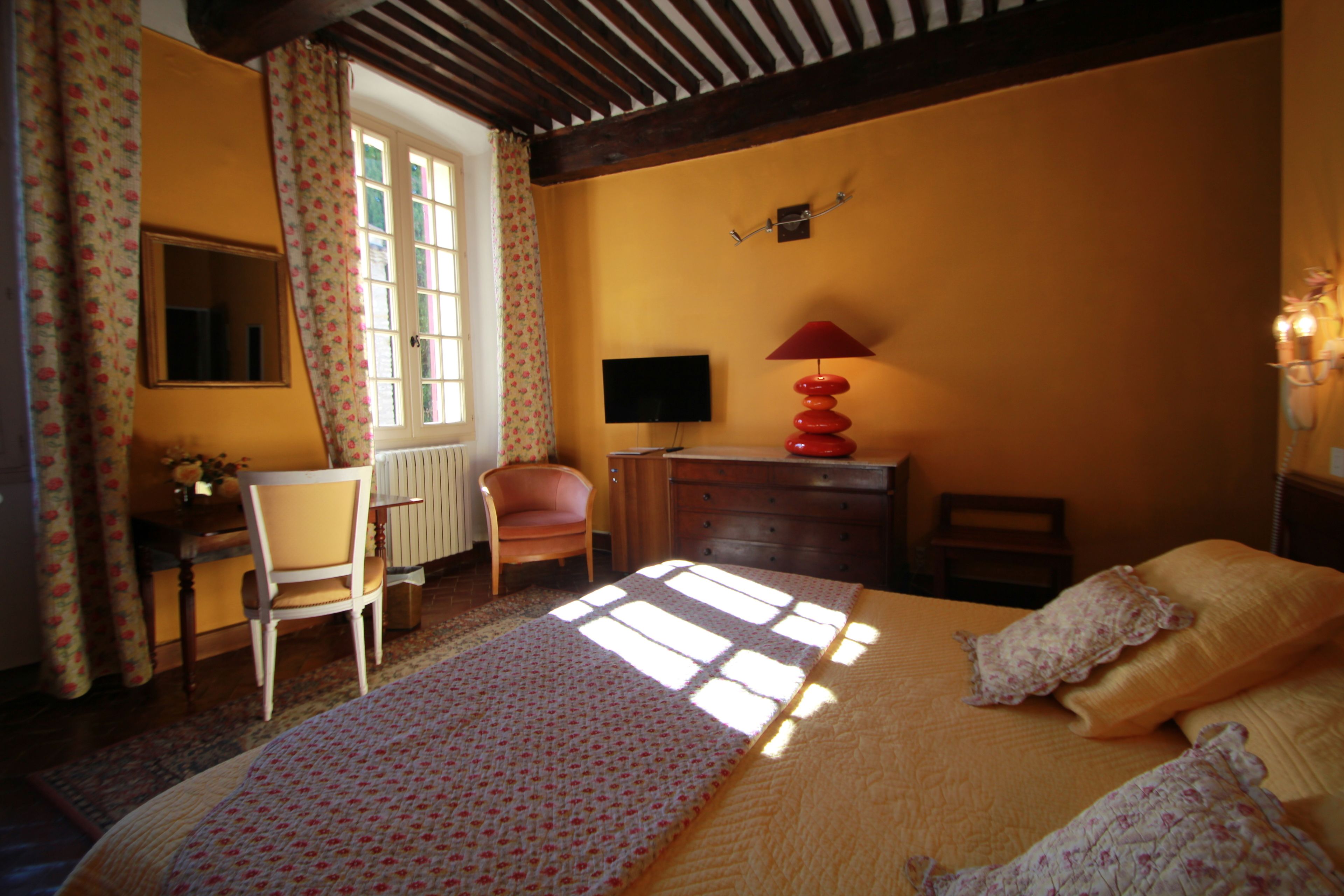 A bedroom with a bed, a desk, a chair, a television, and a lamp.