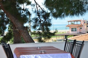 A table with a white tablecloth and two chairs, overlooking a beach and a building with a red roof. - Oren Konak Otel (Burhaniye)