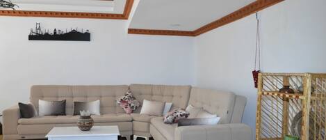Een woonkamer met een beige hoekbank, een witte salontafel en een decoratief wandobject.