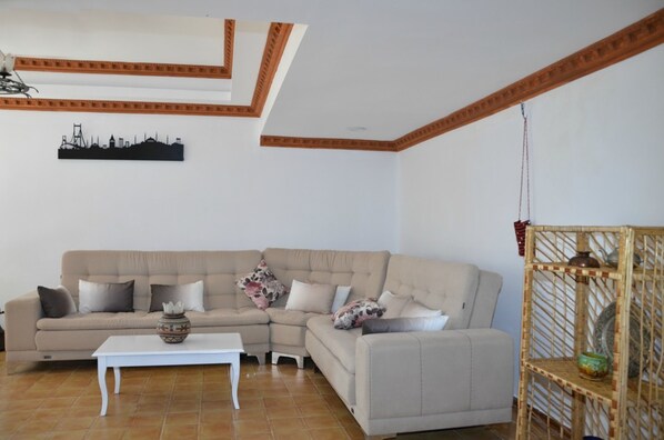 A living room with a beige sectional sofa, a white coffee table, and a decorative wall piece. - Oren Konak Otel (Burhaniye)