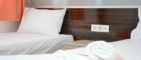 Habitación de hotel con dos camas individuales, cabecero de madera, mesita de noche y toma de corriente.