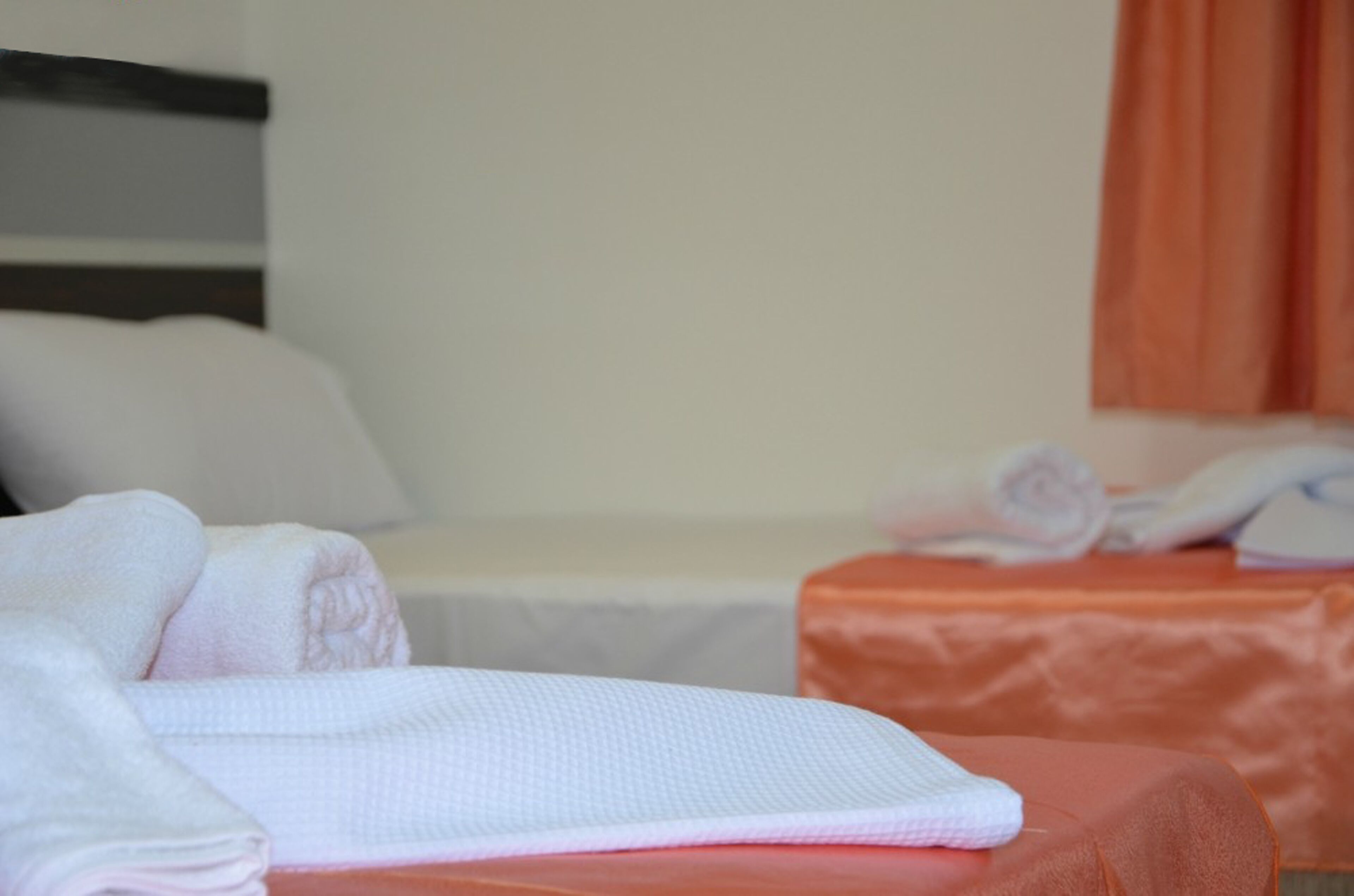 Una habitación de hotel con una cama bien hecha, una mesita de noche con toallas y un ventanal con cortinas.