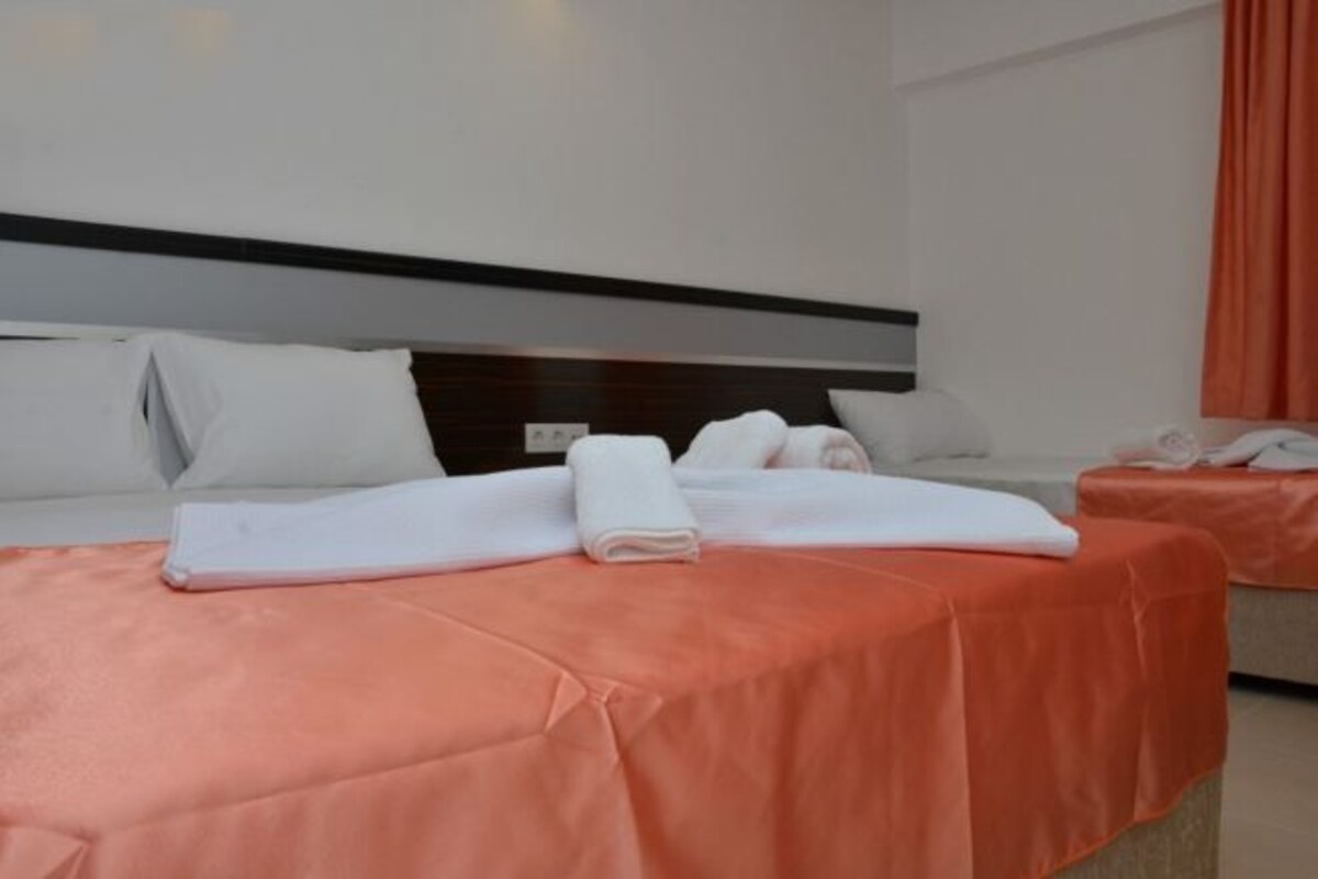 A hotel room with two beds, each with a white headboard, a peach-colored bedspread, and neatly folded white towels.
