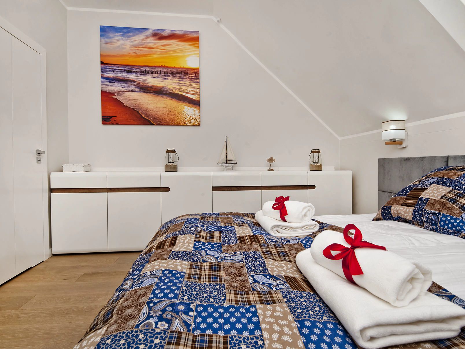 Un dormitorio moderno con una cama grande, vistas al atardecer, un aparador blanco y un pequeño modelo de barco.