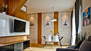 A modern living room with a flat-screen TV, wooden accents, a brick wall, and a dining area with a table and chairs. - Willa Haven BlueApart Jastarnia (Jastarnia)
