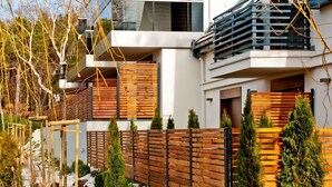 A modern multi-story residential building with a wooden fence, small trees, and a gravel pathway. - Willa Haven BlueApart Jastarnia (Jastarnia)