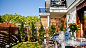 A modern outdoor patio with a glass table, lounge chairs, and a wooden fence. - Willa Haven BlueApart Jastarnia (Jastarnia)