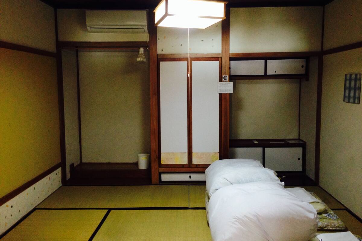 A traditional Japanese-style room with tatami flooring, a futon bed, a shoji screen door, and a ceiling fan.