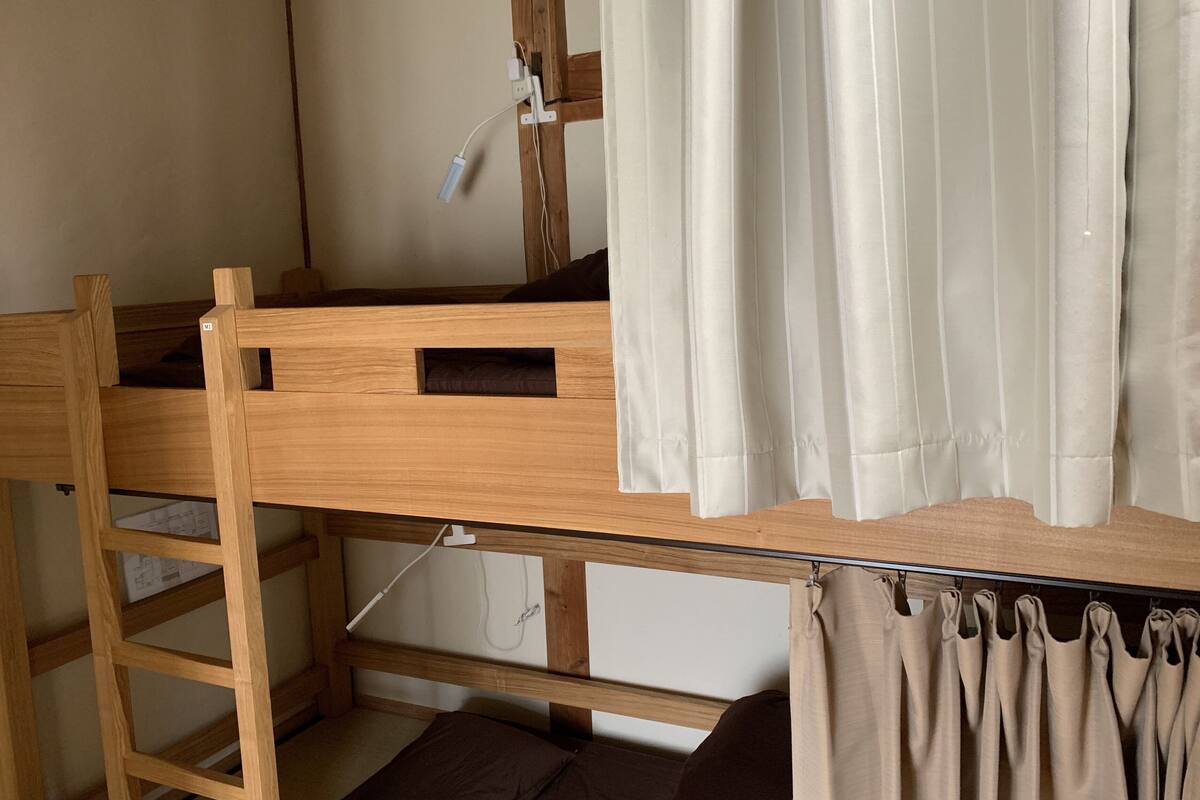 A bunk bed with a ladder, a small shelf, and a curtain.