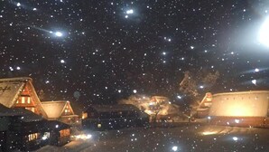 A snowy village scene at night with illuminated buildings and falling snowflakes. - Guest House YAMASHITA-YA - Hostel (Nanto)