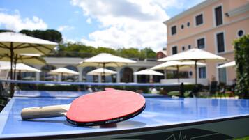 A table tennis table with a paddle, surrounded by umbrellas, with a building in the background.