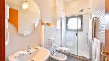 Un bagno moderno con un ampio specchio ovale, un lavandino, un bidet e una cabina doccia in vetro.