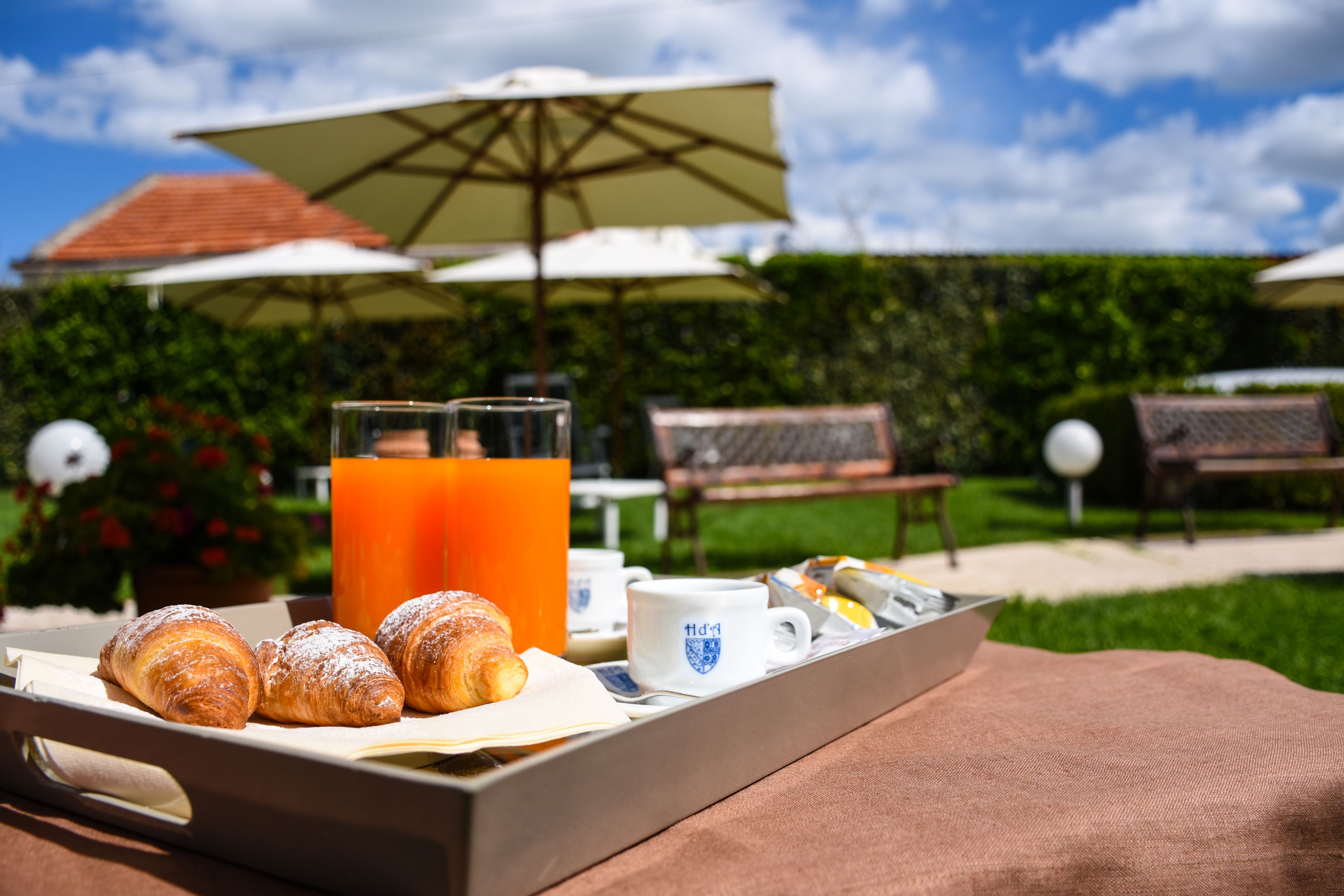 A breakfast tray with croissants, a glass of orange juice, and a coffee mug on a table outdoors.