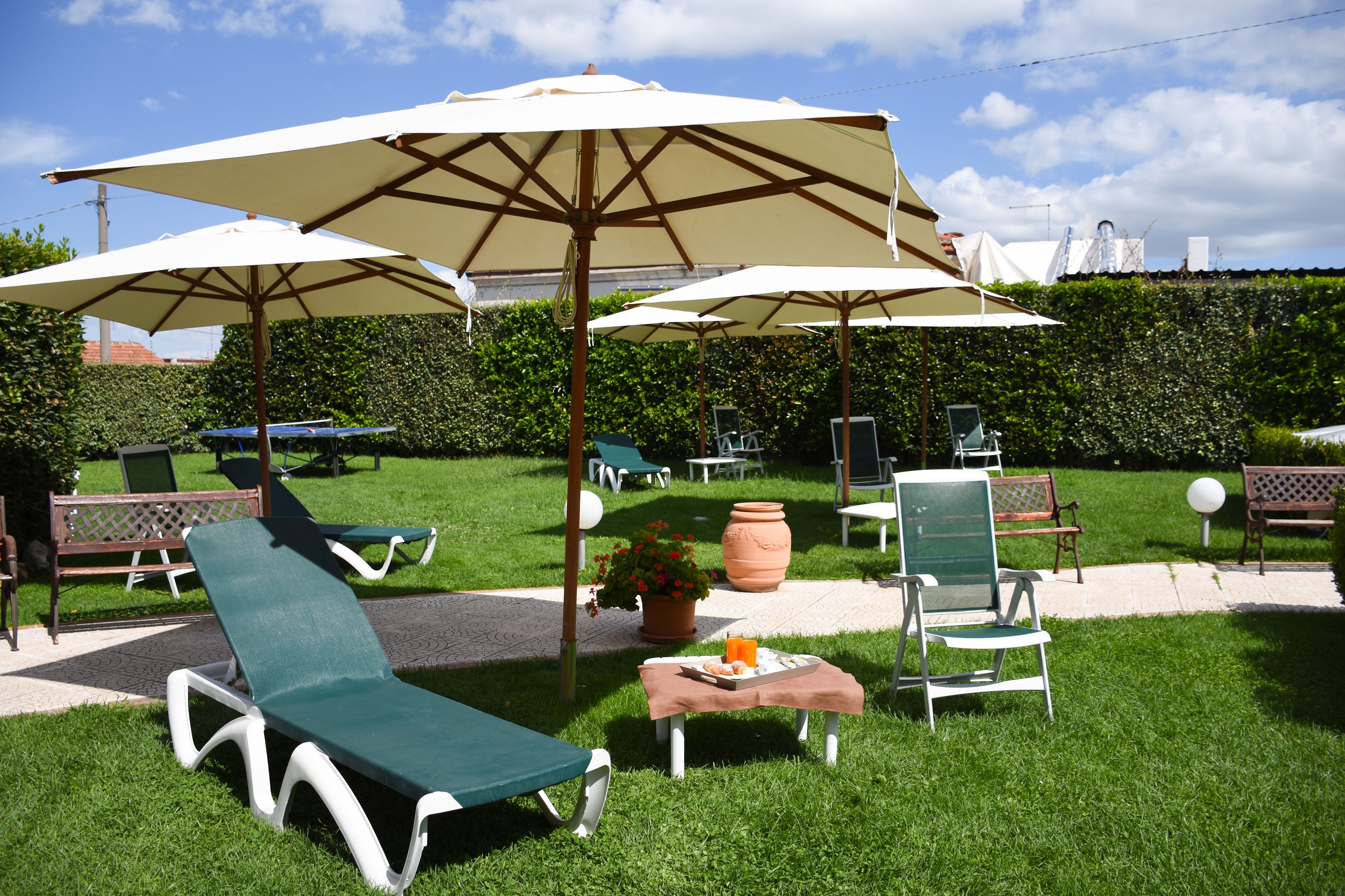 A garden area with lounge chairs, umbrellas, and a table with a drink and snacks.