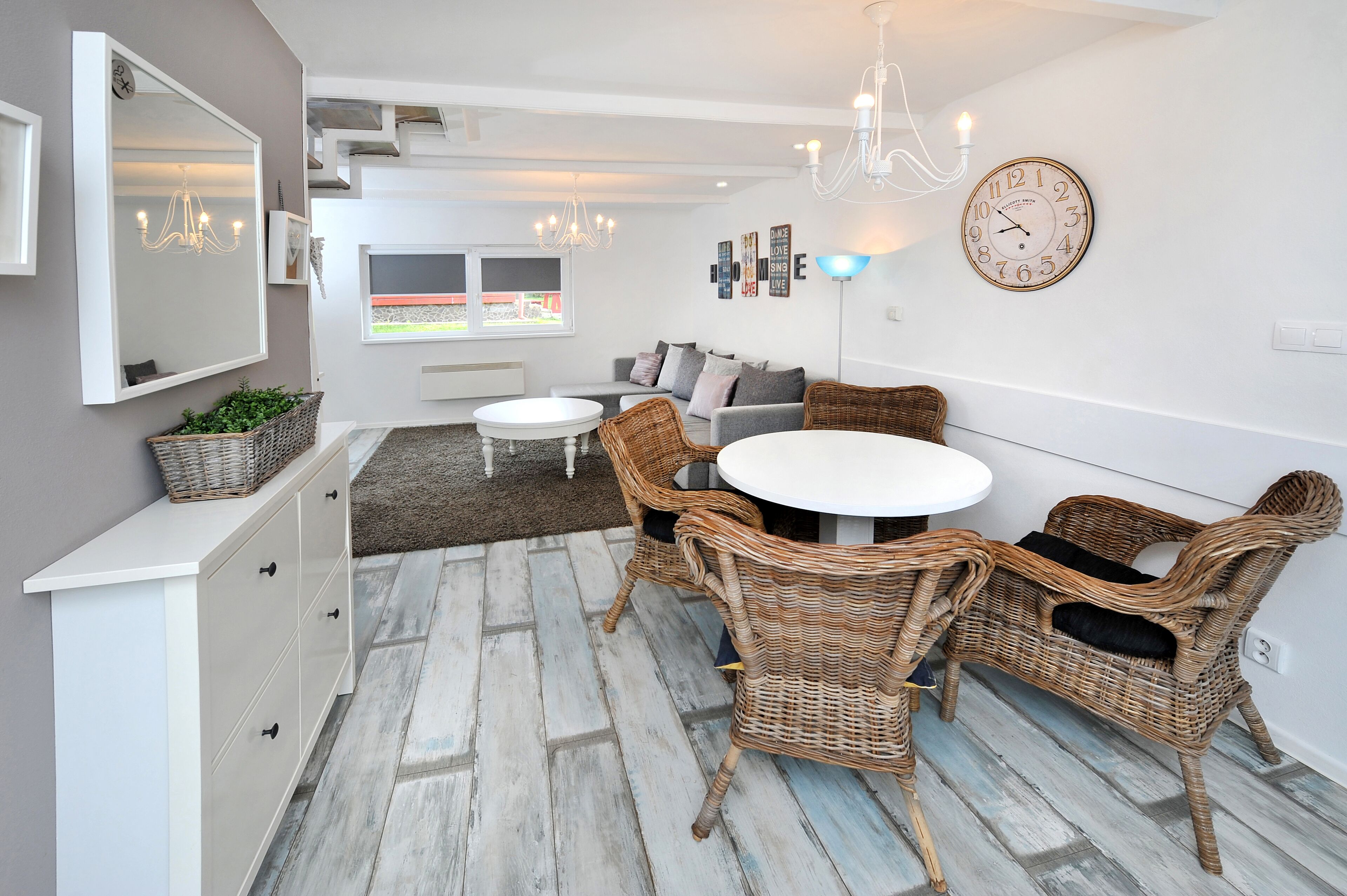 A modern living room with a white sofa, wicker chairs, a round dining table, and a large mirror.