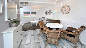 A modern living room with a white sofa, wicker chairs, a round dining table, and a large mirror.