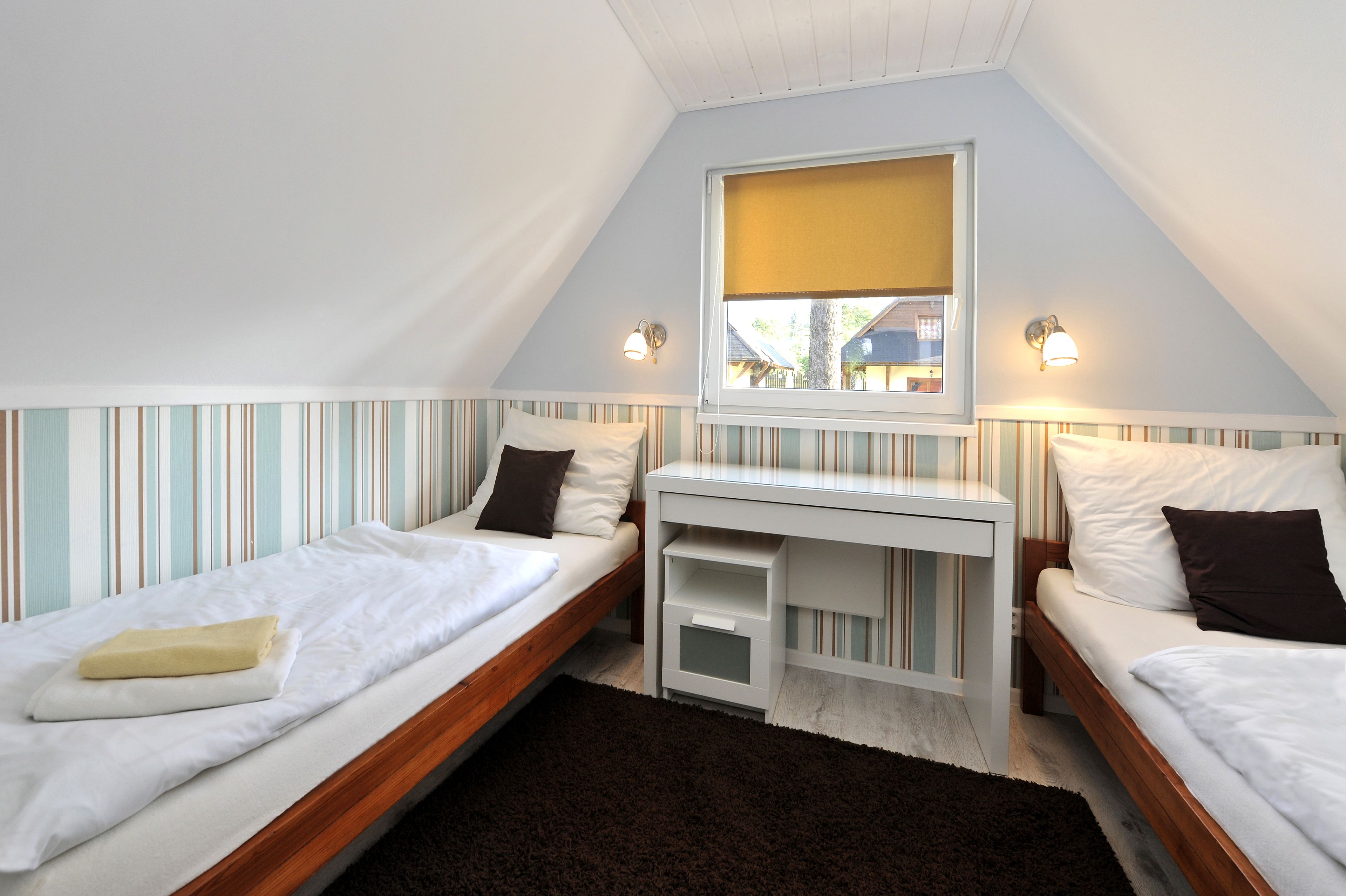 A bedroom with two single beds, a small desk, and a window with blinds.