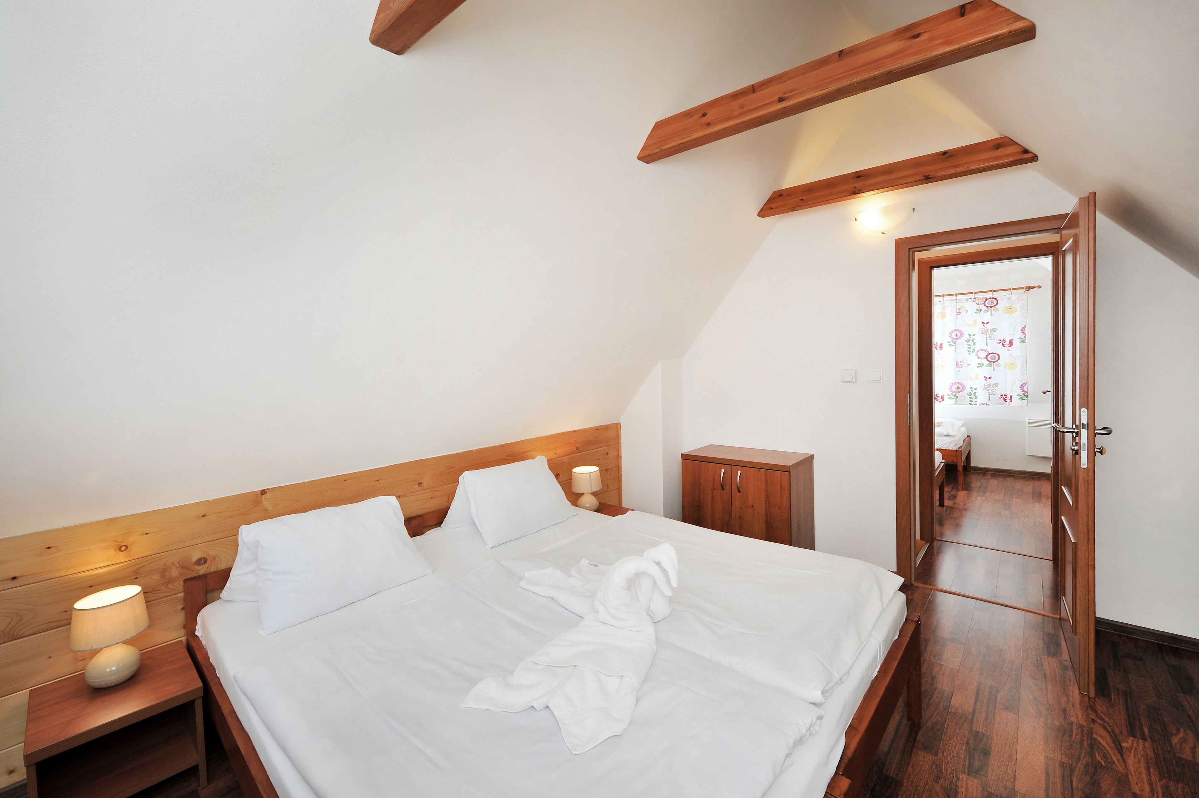A neatly made bed with white linens, a wooden headboard, a bedside lamp, and a wooden wardrobe.