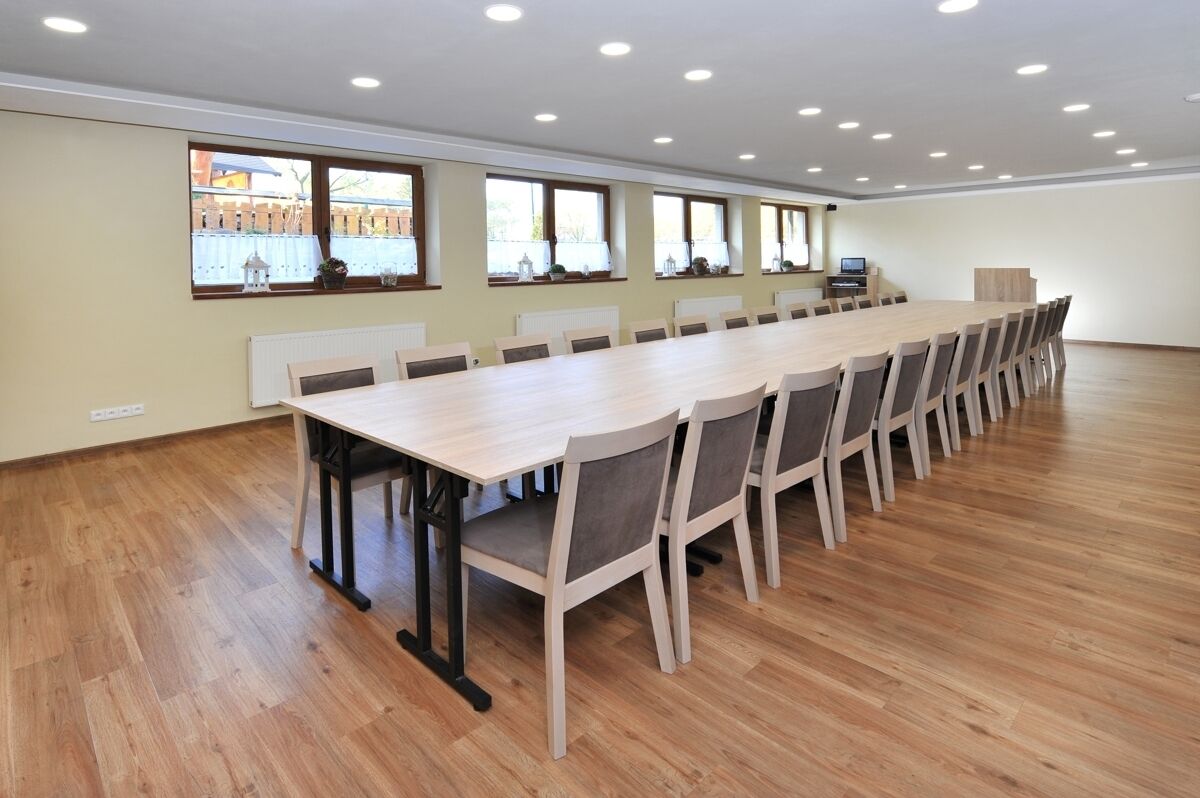 A large conference room with a long table and chairs, large windows with blinds, and a wooden floor.