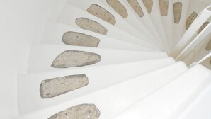 Uma escada em espiral com degraus brancos e bordas semelhantes a pedra.