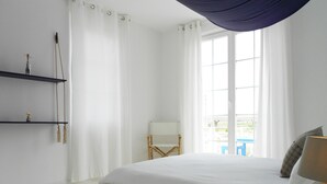 Une chambre avec un grand lit, une chaise, une table et une fenêtre avec des rideaux.
