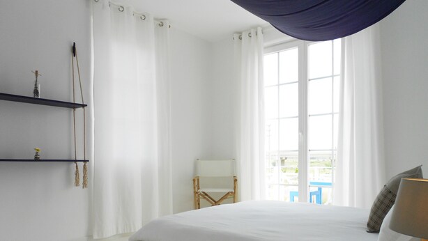 Quarto com uma cama grande, uma cadeira, uma mesa e uma janela com cortinas.