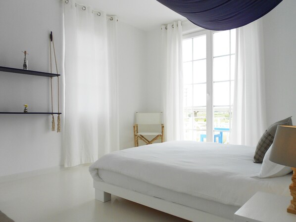 A bedroom with a large bed, a chair, a table, and a window with curtains. - Manta Alacati (Cesme)