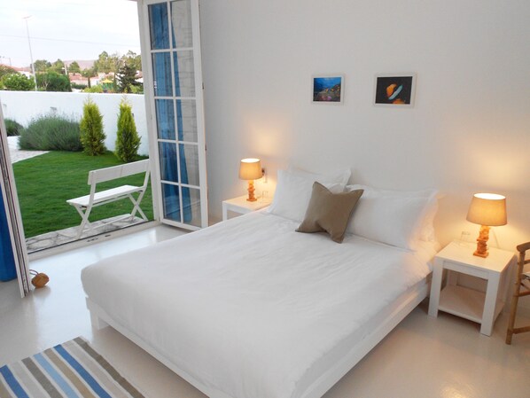 Un dormitorio con una cama grande, dos mesitas de noche con lámparas, una ventana con vistas a zonas verdes y dos pequeños cuadros en la pared.