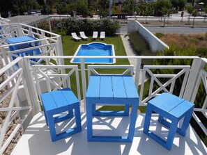 Uma área de piscina com mesas e cadeiras azuis, cercada por guarda-corpos brancos.
