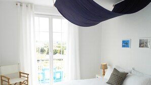 Quarto com cama, cadeira, mesa de cabeceira e vista para o exterior.