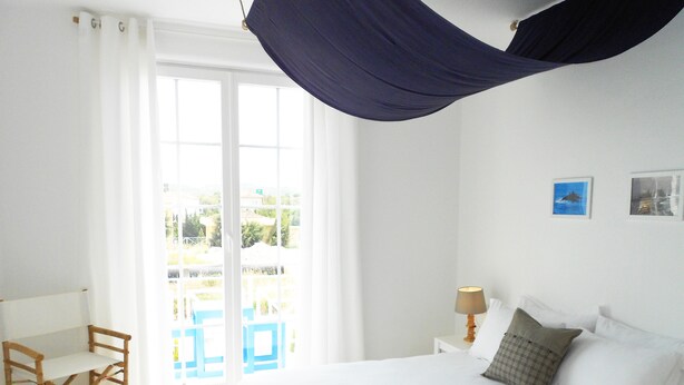 Une chambre à coucher avec un lit, une chaise, une table de chevet et une vue sur l’extérieur.