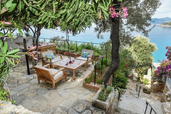 A stone patio with outdoor furniture, a view of the sea, and lush greenery. - Beyaz Yunus Hotel - Adults only (Fethiye)