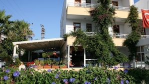 Un edifici de diversos pisos amb balcons, un vestíbul cobert i diverses plantes i flors al primer pla.