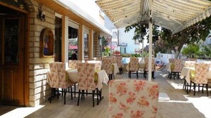 Zona d'un cafè a l'aire lliure amb taules i cadires, coberta per una ombrellera amb ratlles, i vista al carrer i els edificis al fons.