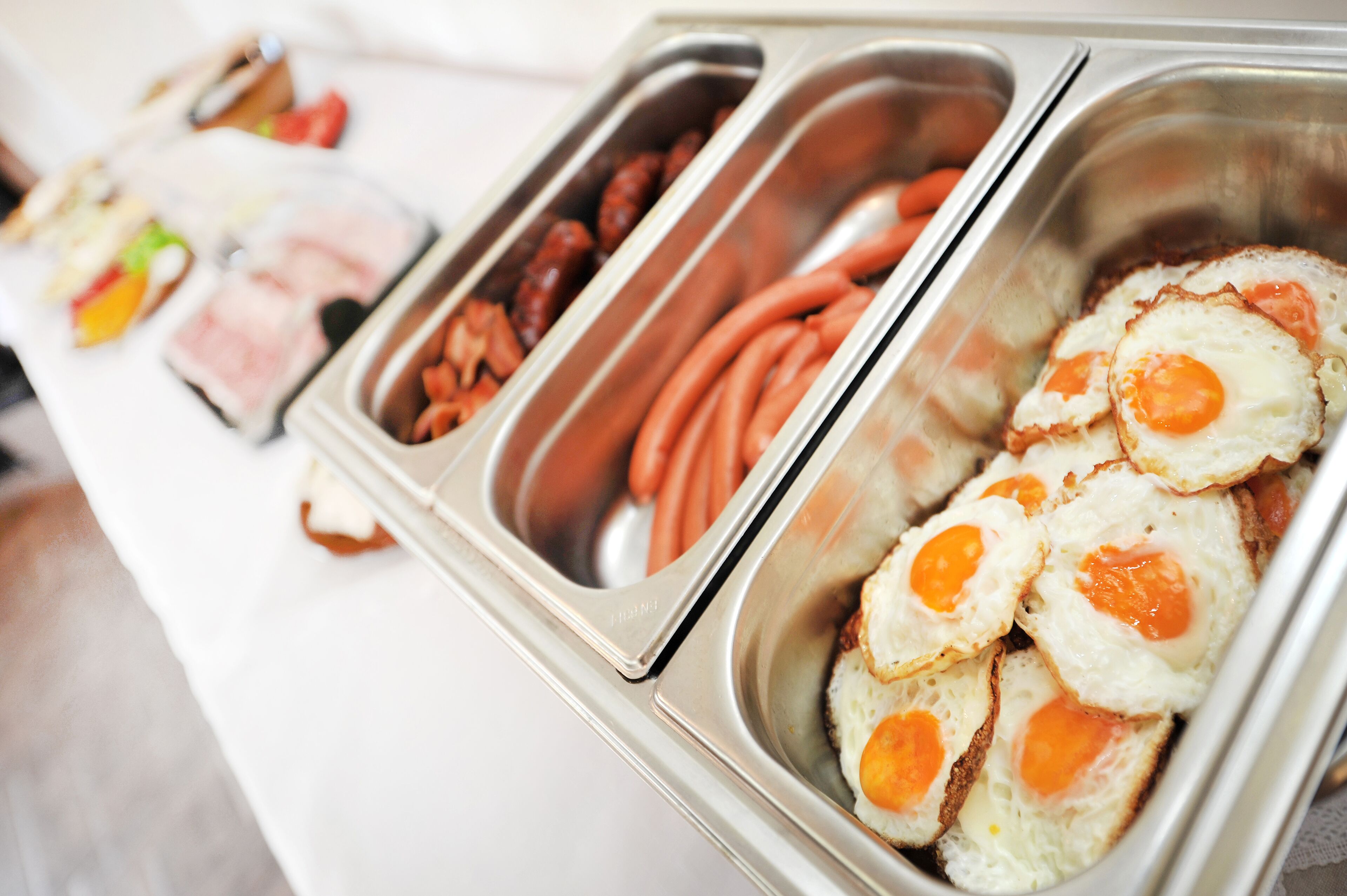 A buffet line with various food options including eggs, sausages, and other meats.