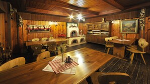A wooden dining area with a long table, chairs, a fireplace, and a kitchen area with cabinets and a painting on the wall. - APLEND Domčeky Tatry Holiday (Velky Slavkov)