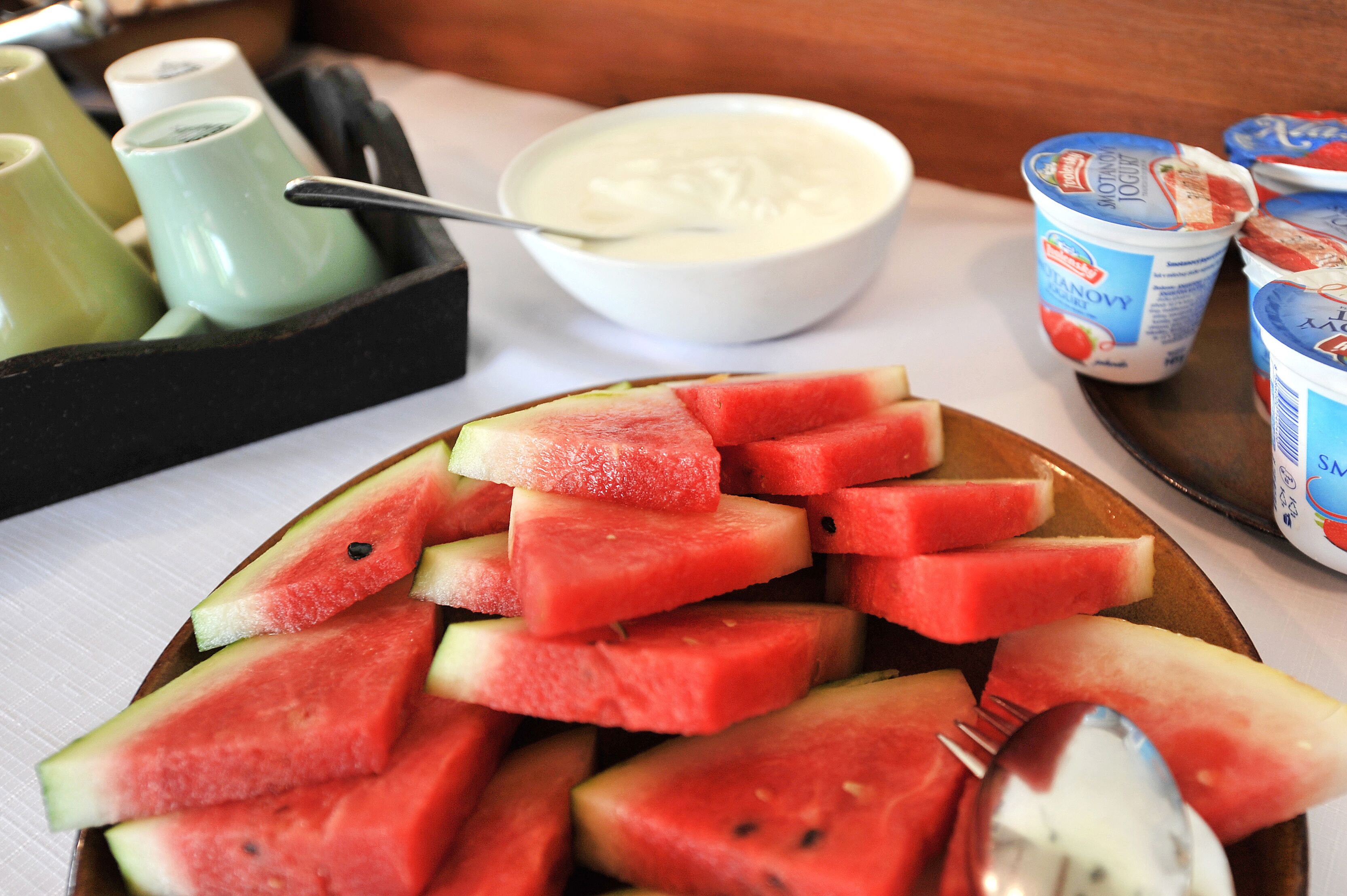 A plate of watermelon slices, a bowl of yogurt, and yogurt cups on a table.