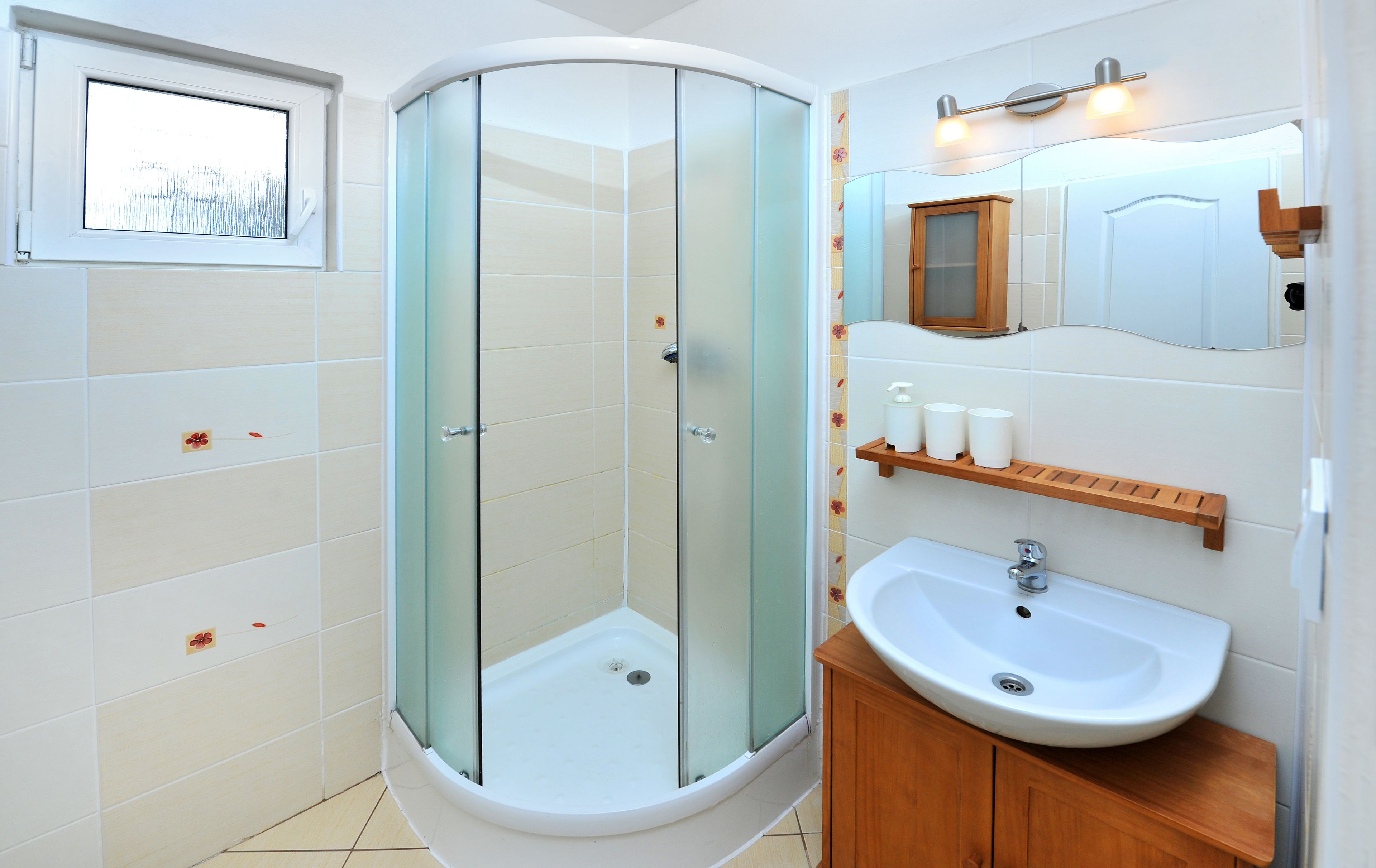 Un bagno moderno con doccia vetro, lavandino bianco e mobile contenitore in legno.