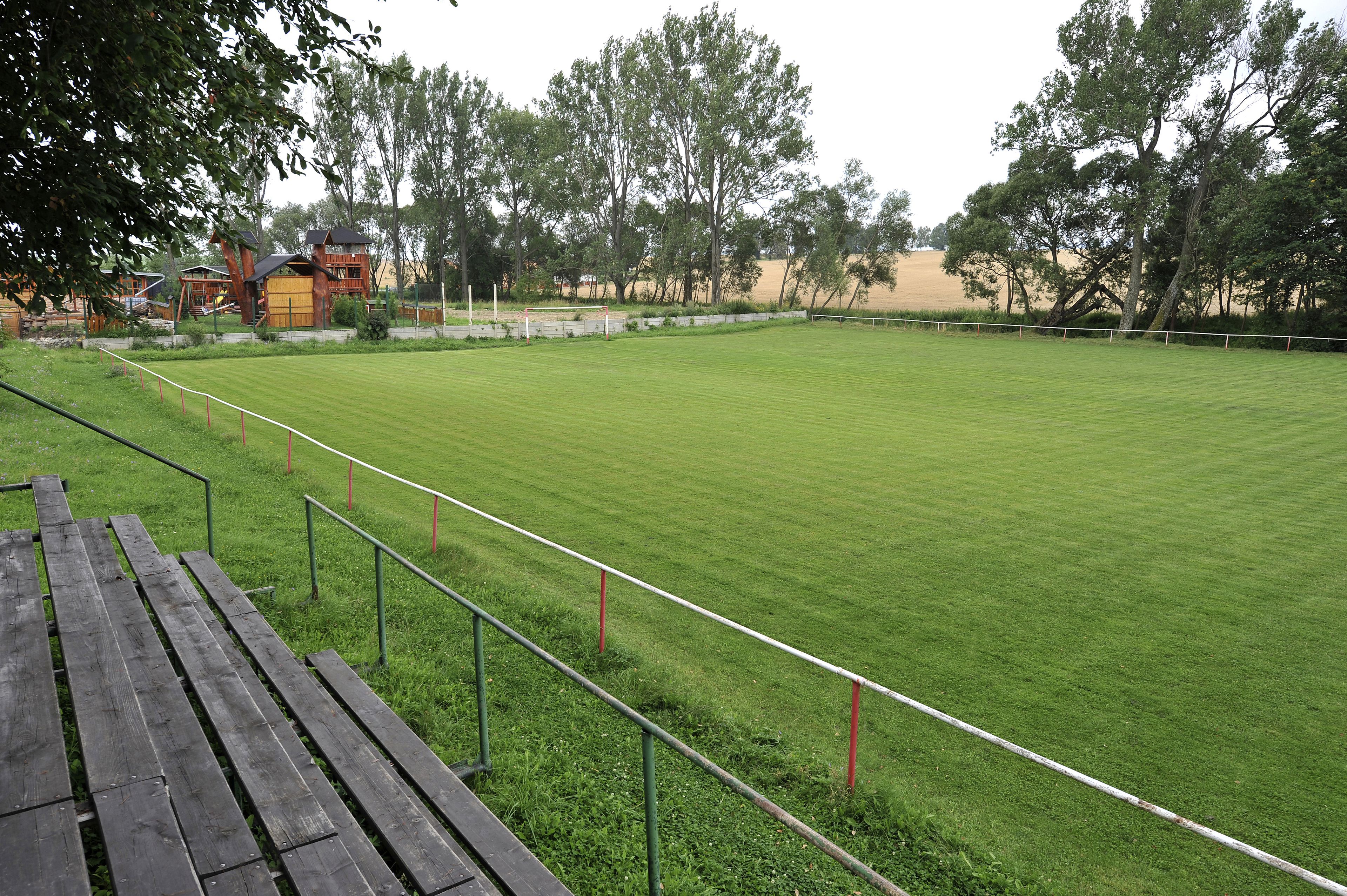 A grassy sports field with a wooden bench and metal railings.