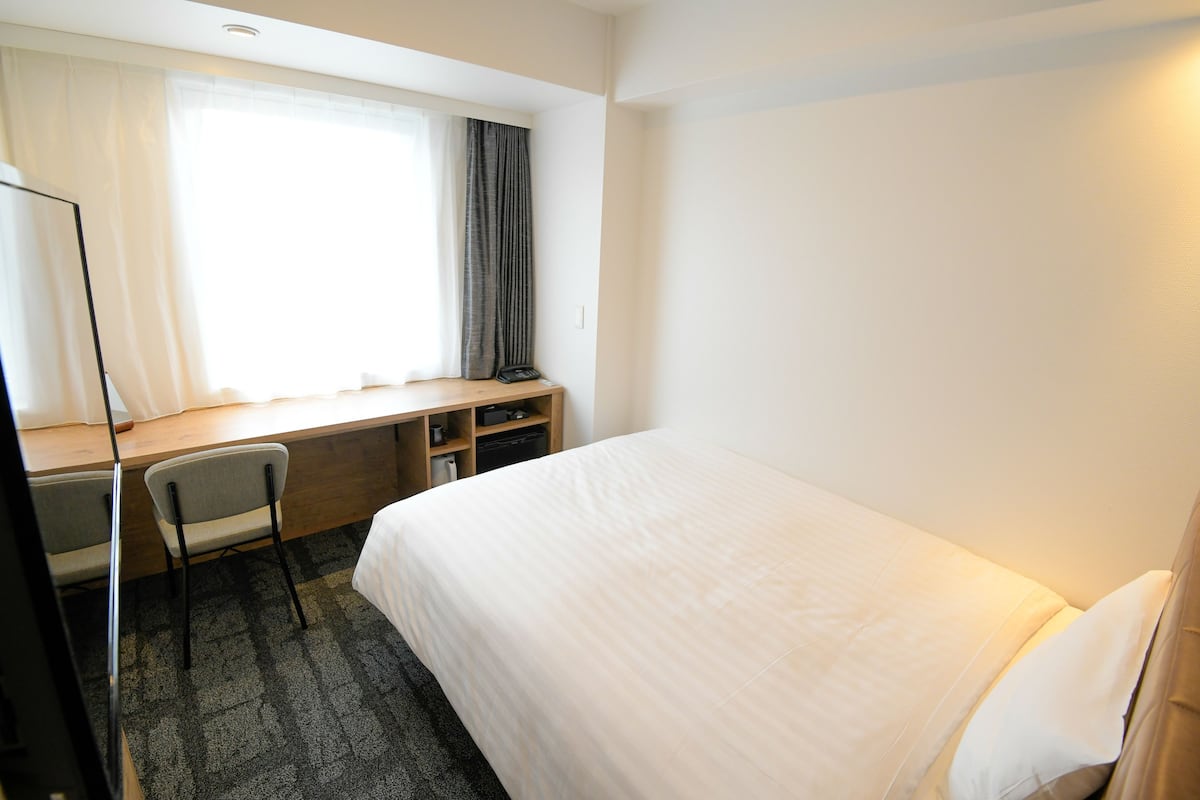 A hotel room with a bed, a desk, a chair, and a window with curtains.