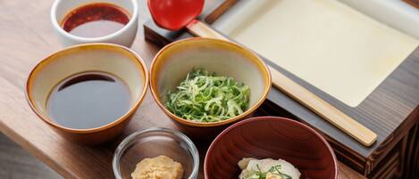 A traditional Japanese meal setup with bowls of soup, pickled vegetables, and dumplings, along with a small bowl of sauce and a red bowl with a lid.
