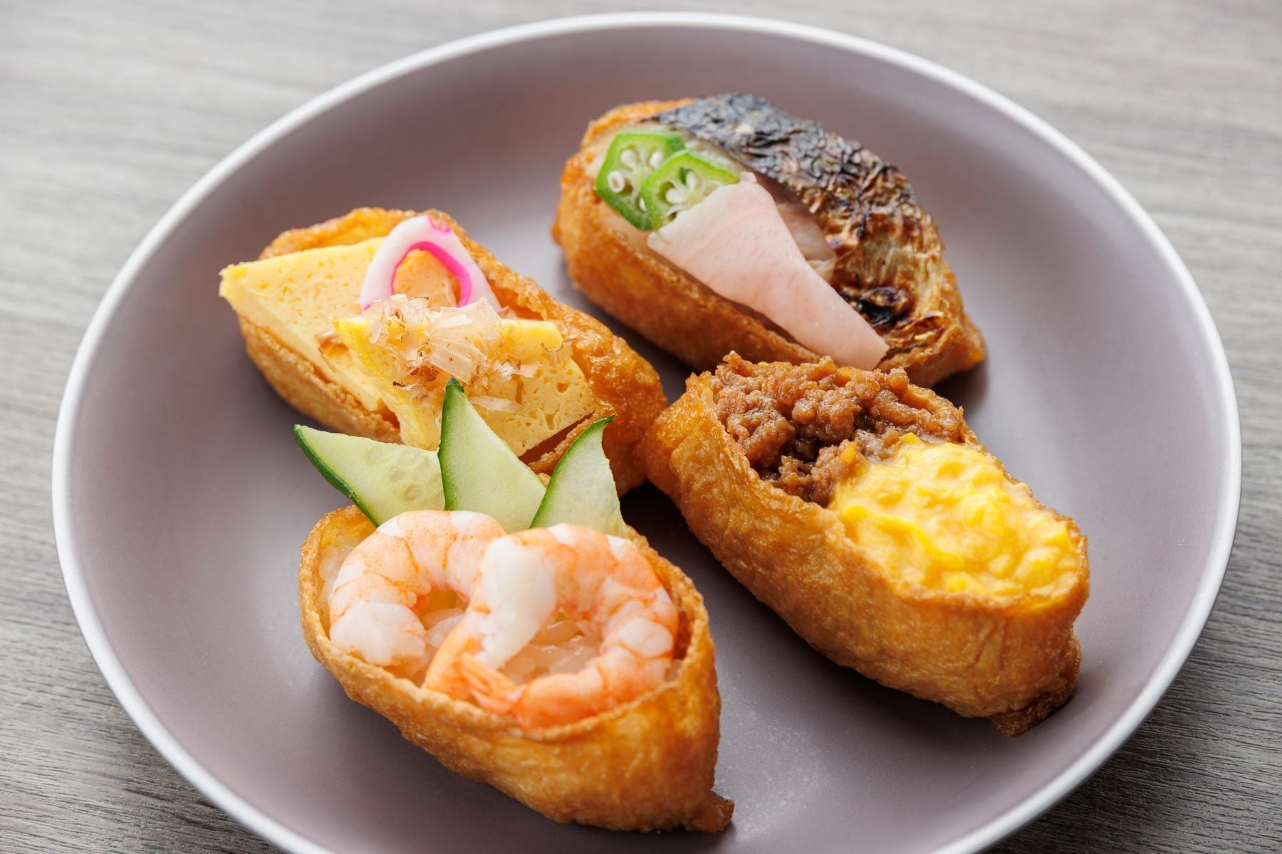 Un plato con cuatro diferentes tipos de comida, incluyendo camarones, pescado y otros mariscos, servido sobre un plato gris.