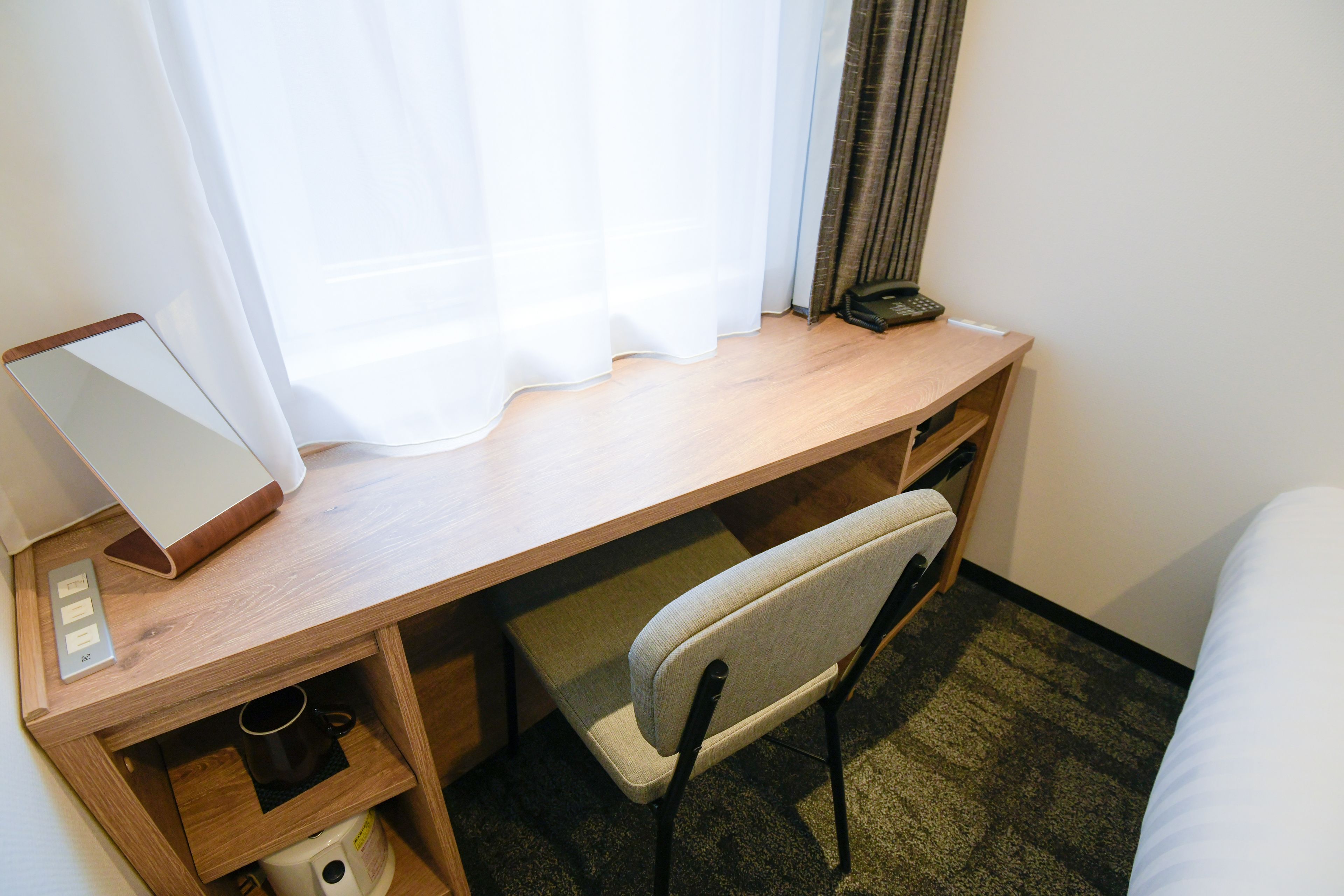 Una habitación de hotel con un escritorio de madera, una silla, una mesita de noche y una cama.